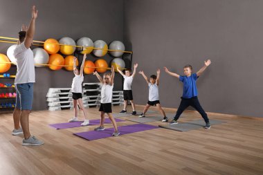 Sevimli küçük çocuklar ve eğitmen okul spor salonunda fiziksel egzersiz yapıyor. Sağlıklı yaşam tarzı