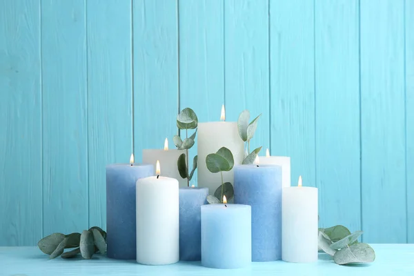 Set brennender Kerzen mit Eukalyptus auf dem Tisch vor hellblauem Holzhintergrund — Stockfoto