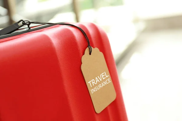 Röd resväska med rese försäkringens etikett inomhus, plats för text — Stockfoto