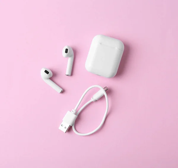 Fones de ouvido sem fio modernos e caixa de carregamento com cabo em fundo rosa, flat lay — Fotografia de Stock