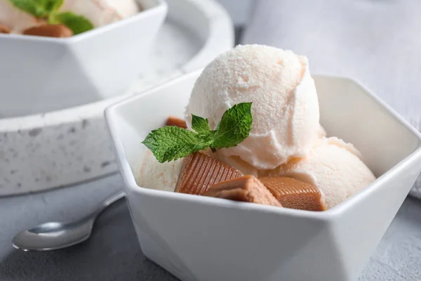 Tigela de sorvete com doces de caramelo e hortelã na mesa cinza claro, close-up — Fotografia de Stock