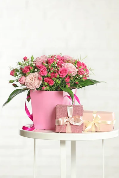 Belo buquê de flores e caixas de presente na mesa contra fundo leve — Fotografia de Stock