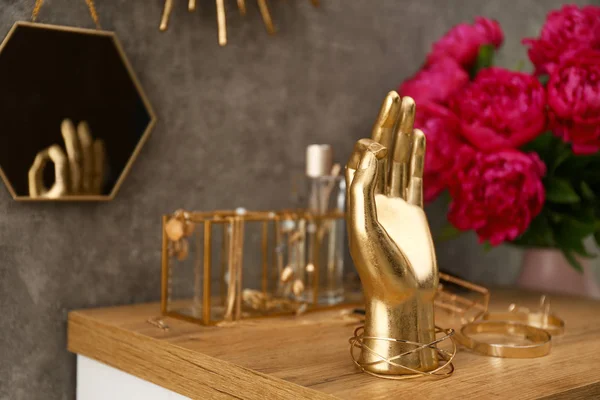 Тримач у формі золотої руки, прикраси та аксесуари на туалетному столику біля сірої стіни. Простір для тексту — стокове фото