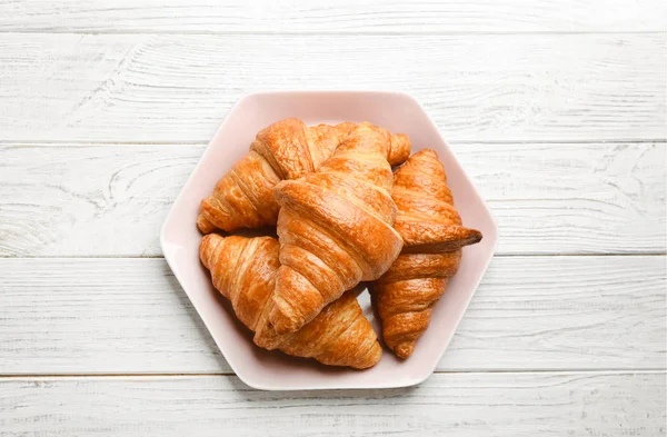 Placa con sabrosos croissants sobre fondo de madera blanca, vista superior. Pastelería francesa — Foto de Stock