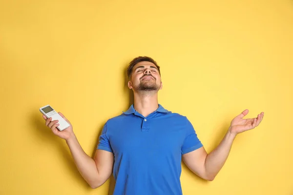 Jovem feliz com ar condicionado controle remoto no fundo amarelo — Fotografia de Stock