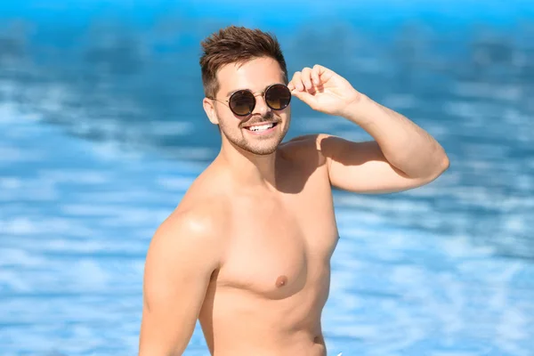 Bonito jovem com óculos de sol perto da piscina no dia ensolarado — Fotografia de Stock
