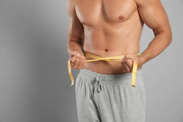 Homem jovem com corpo magro usando fita métrica em fundo cinza, vista close-up. Espaço para texto — Fotografia de Stock