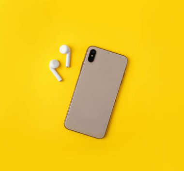 Kablosuz kulaklık ve cep telefonu sarı arka plan, düz yatıyordu. Metin için alan