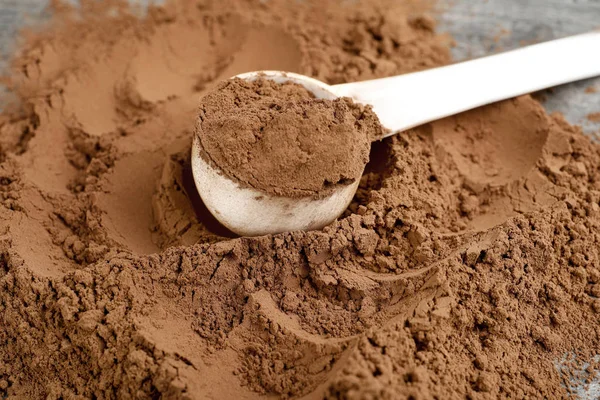 Stapel chocolade proteïne poeder en schep op grijze tafel, close-up — Stockfoto