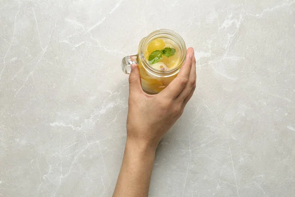 Mujer sosteniendo tarro Mason de cóctel de bola de melón con menta en la mesa de mármol gris claro, vista superior —  Fotos de Stock