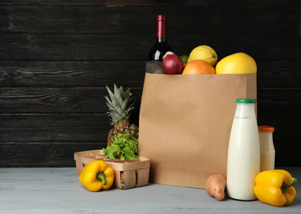 Paper bag with groceries on wooden table against dark background. Space for text