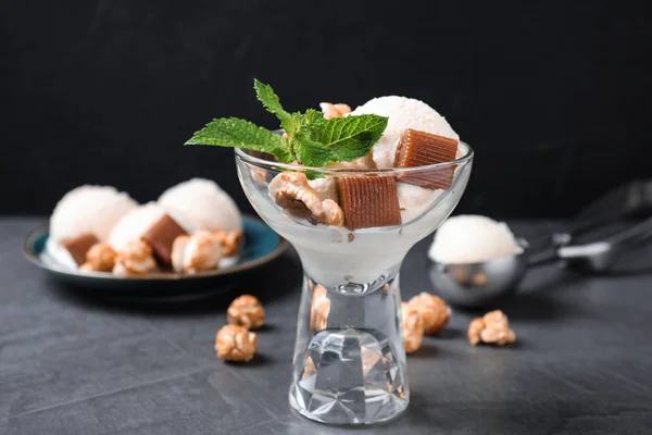 Tigela de vidro de sorvete com doces de caramelo, pipoca e hortelã na mesa cinza — Fotografia de Stock