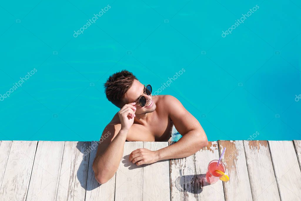 Handsome young man with refreshing cocktail in swimming pool on sunny day, above view