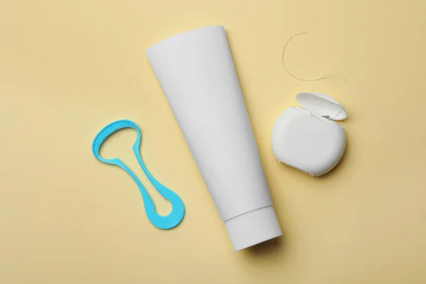 Tongue cleaner, tooth paste and dental floss on color background, flat lay