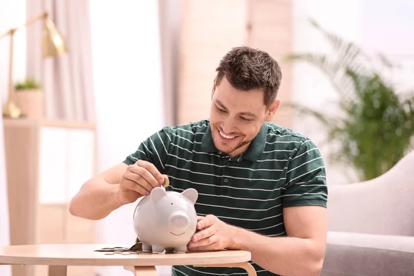 Man with piggy bank and money at home — Stock Photo, Image