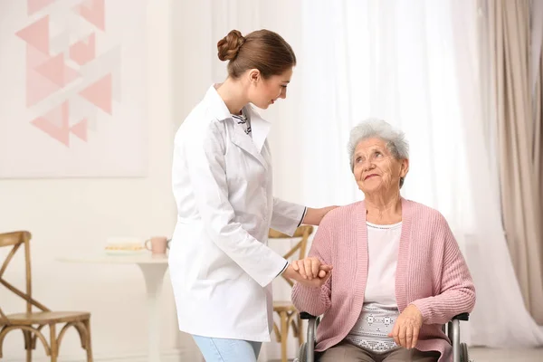 Enfermera asistiendo a anciana en silla de ruedas en interiores — Foto de Stock