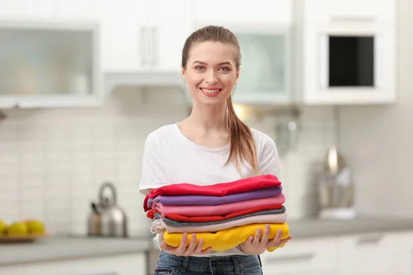 Женщина, держащая сложенную чистую одежду на кухне. День прачечной — стоковое фото