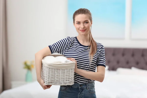 Mujer sosteniendo cesta de mimbre con toallas limpias dobladas en el dormitorio. Día de lavandería — Foto de Stock