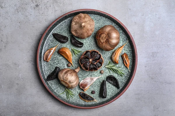 Plate with black garlic on grey table, top view