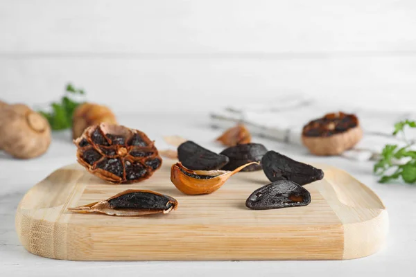 Wooden board with black garlic on white table