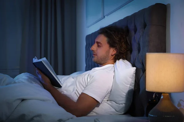 Schöner junger Mann, der nachts in einem dunklen Raum Bücher liest. Schlafenszeit — Stockfoto