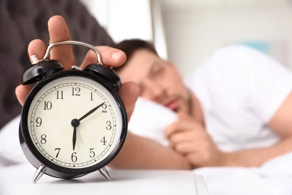 Omul somnoros opreşte ceasul deşteptător pe noptieră. Dormitor — Fotografie, imagine de stoc