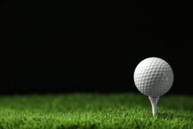 Siyah arka plana karşı suni çim üzerinde tee ile golf topu, metin için alan