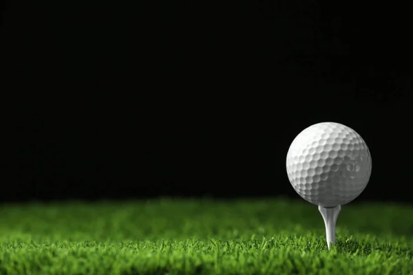 Bola de golfe com tee na grama artificial contra fundo preto, espaço para texto — Fotografia de Stock