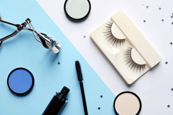 Flat lay composition with false eyelashes and other makeup products on color background