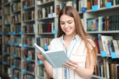 Kütüphanede raf ünitesi yakınında kitap okuyan genç kadın