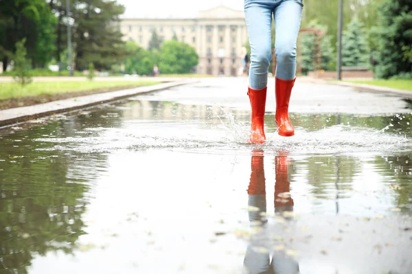 Mulher com botas de borracha vermelha saltando na poça, close-up. Tempo chuvoso — Fotografia de Stock