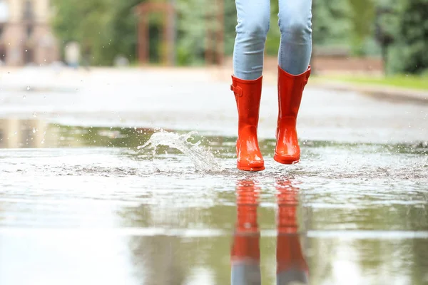 Γυναίκα με κόκκινες λαστιχένιες μπότες να πηδούν στην λακκούβα, κοντινό. Βροχερός καιρός — Φωτογραφία Αρχείου