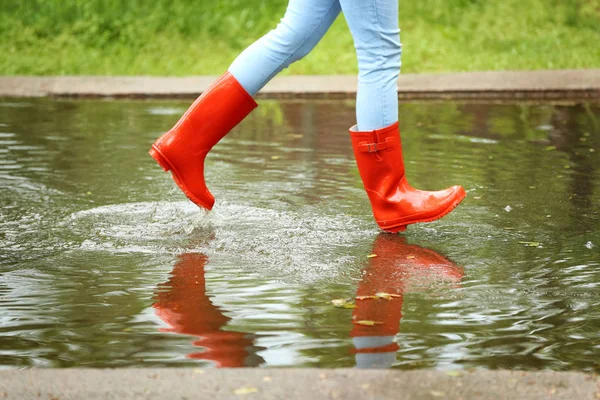 赤いゴムのブーツを持つ女性は、水たまりで実行され、クローズアップ。雨天 — ストック写真