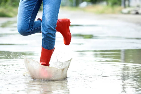 赤いゴムのブーツを持つ女性は、水たまりで実行され、クローズアップ。雨天 — ストック写真