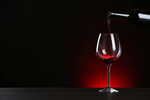 Versare il vino dalla bottiglia al bicchiere sul tavolo sullo sfondo scuro, spazio per il testo — Foto Stock