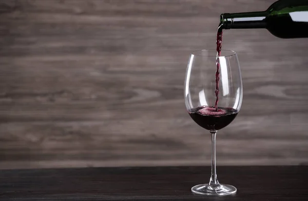 Despejando vinho de garrafa em vidro na mesa contra fundo de madeira, espaço para texto — Fotografia de Stock