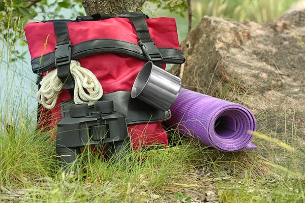 Rucksack und Campingausrüstung auf Gras in der Nähe von Bäumen in der Wildnis — Stockfoto