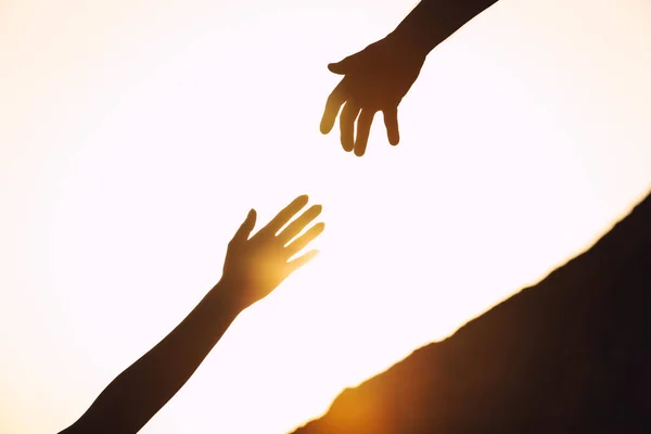 Silhouettes of man and woman helping each other to climb on hill against sunset, closeup