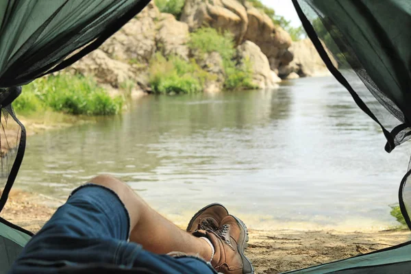 Young man resting in camping tent on riverbank, view from inside — Stock Photo, Image