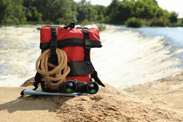 Mochila y equipo de camping en piedra cerca del río. Espacio para texto —  Fotos de Stock