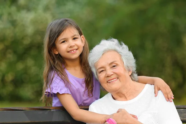 Petite fille et sa grand-mère étreignant sur le banc dans le parc — Photo