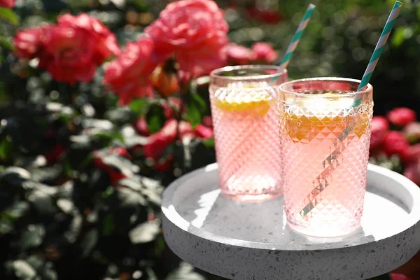 Bicchieri di limonata rosa su tavolo bianco in roseto. Spazio per testo — Foto Stock