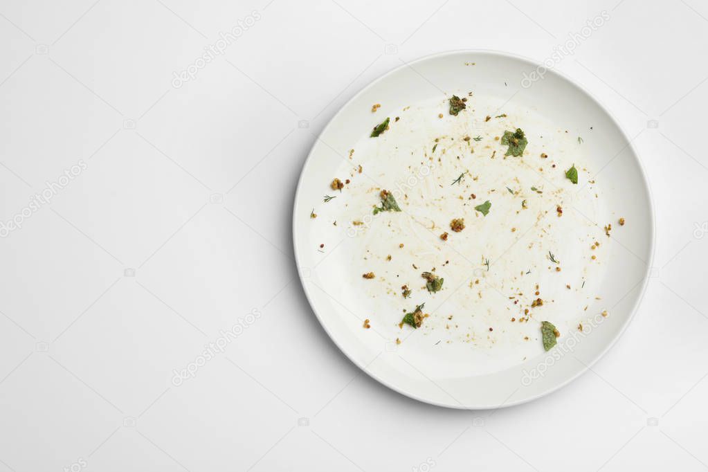 Dirty plate with food leftovers on white background, top view