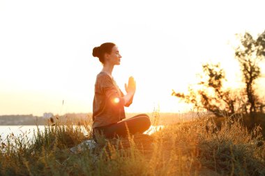 Genç kadın gün batımında açık havada yoga yapıyor. Zen meditasyonu