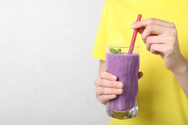 Kadın ışık arka plan üzerinde lezzetli yaban mersini smoothie cam tutan, closeup