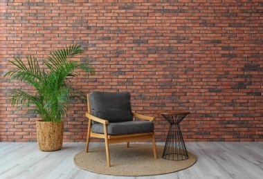 Tuğla duvara yakın şık gri koltuk ve saksı bitki ile modern oda iç