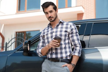 Açık havada lüks araba yakınında kahve fincan ile çekici genç adam