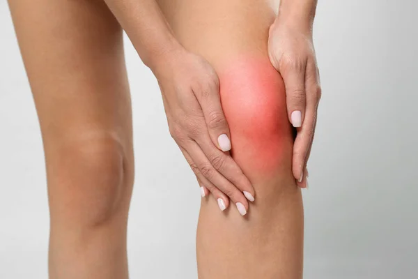 У женщины проблемы с коленом на сером фоне, крупный план — стоковое фото