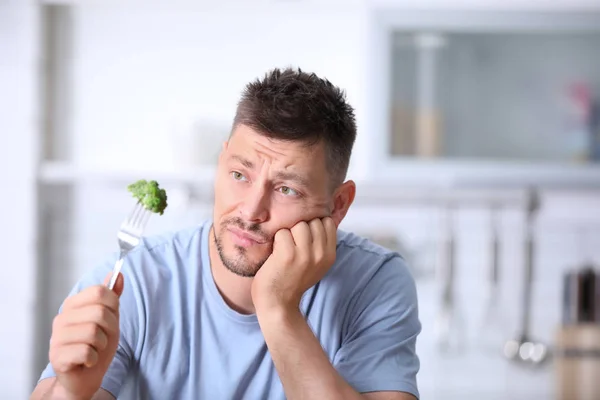 在厨房里看花椰菜在叉子上的不快乐的人的肖像 — 图库照片