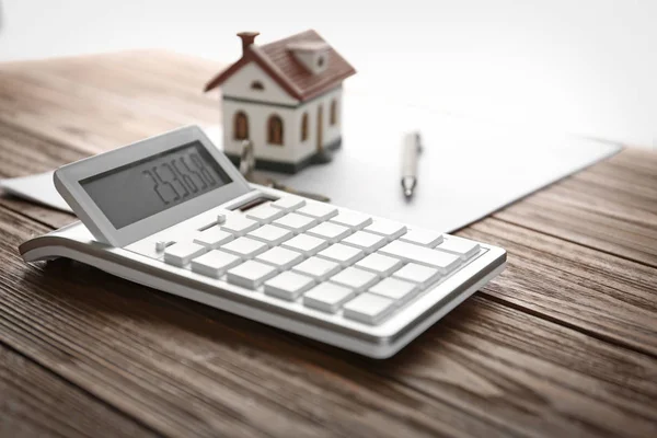 Kalkylator, hus modell, penna och dokument på träbord. Fastighetsmäklaren arbetsplats — Stockfoto
